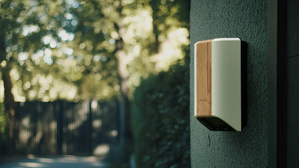 Andersen Quartz EV charger in light cream and wood finish installed on a textured green exterior wall, blending with a leafy residential driveway.”